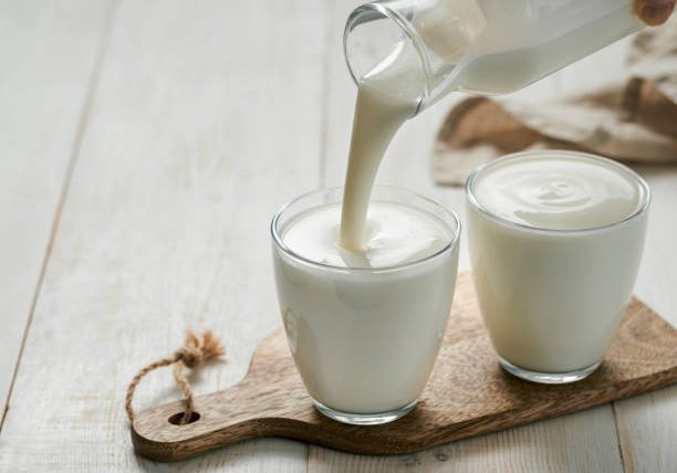 Pouring homemade kefir, buttermilk or yogurt with probiotics. Yogurt flowing from glass bottle on white wooden background. Probiotic cold fermented dairy drink. Trendy food and drink. Copy space left