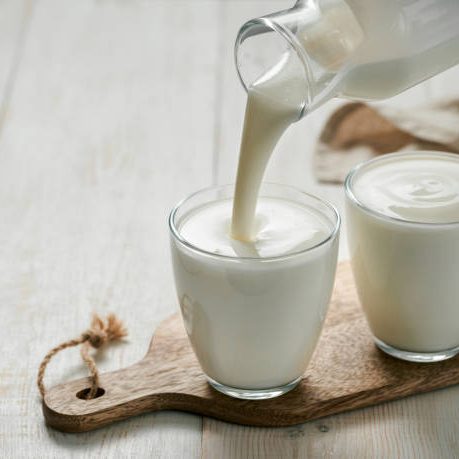 Pouring homemade kefir, buttermilk or yogurt with probiotics. Yogurt flowing from glass bottle on white wooden background. Probiotic cold fermented dairy drink. Trendy food and drink. Copy space left